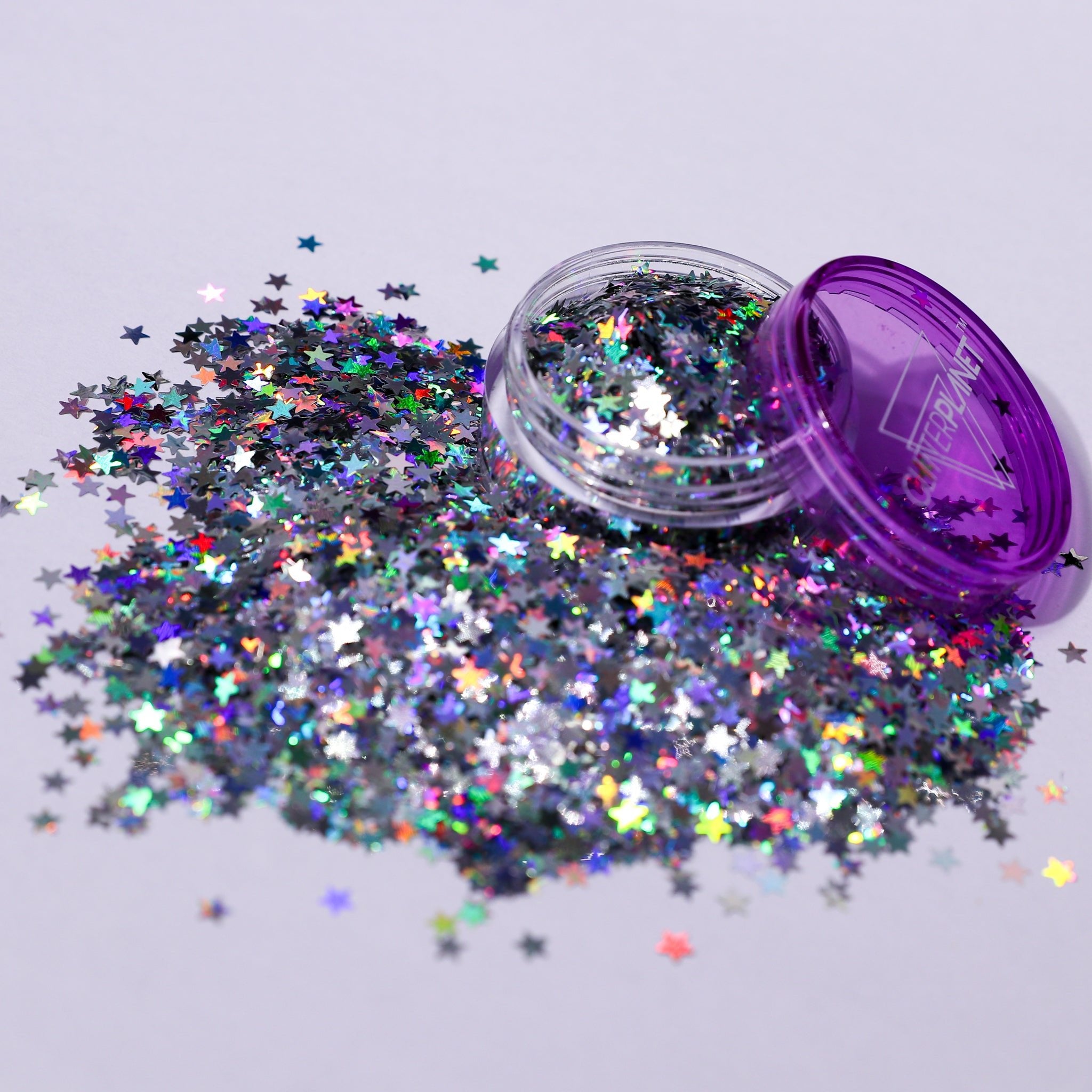 Star-shaped glitter spilling out of a purple container on a light gray background