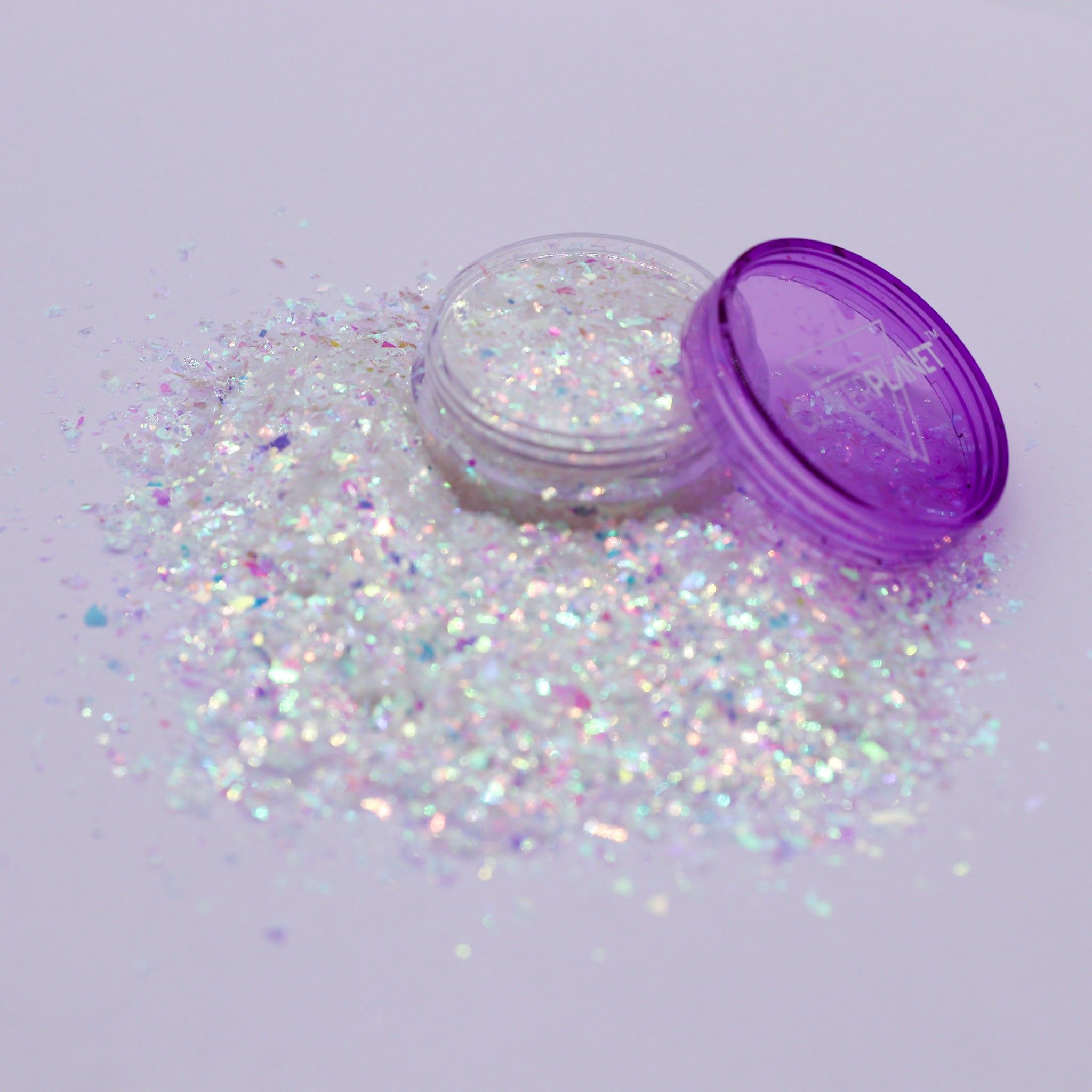 Iridescent glitter spilling out of a purple container on a light gray background