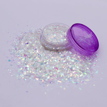 Iridescent glitter spilling out of a purple container on a light gray background