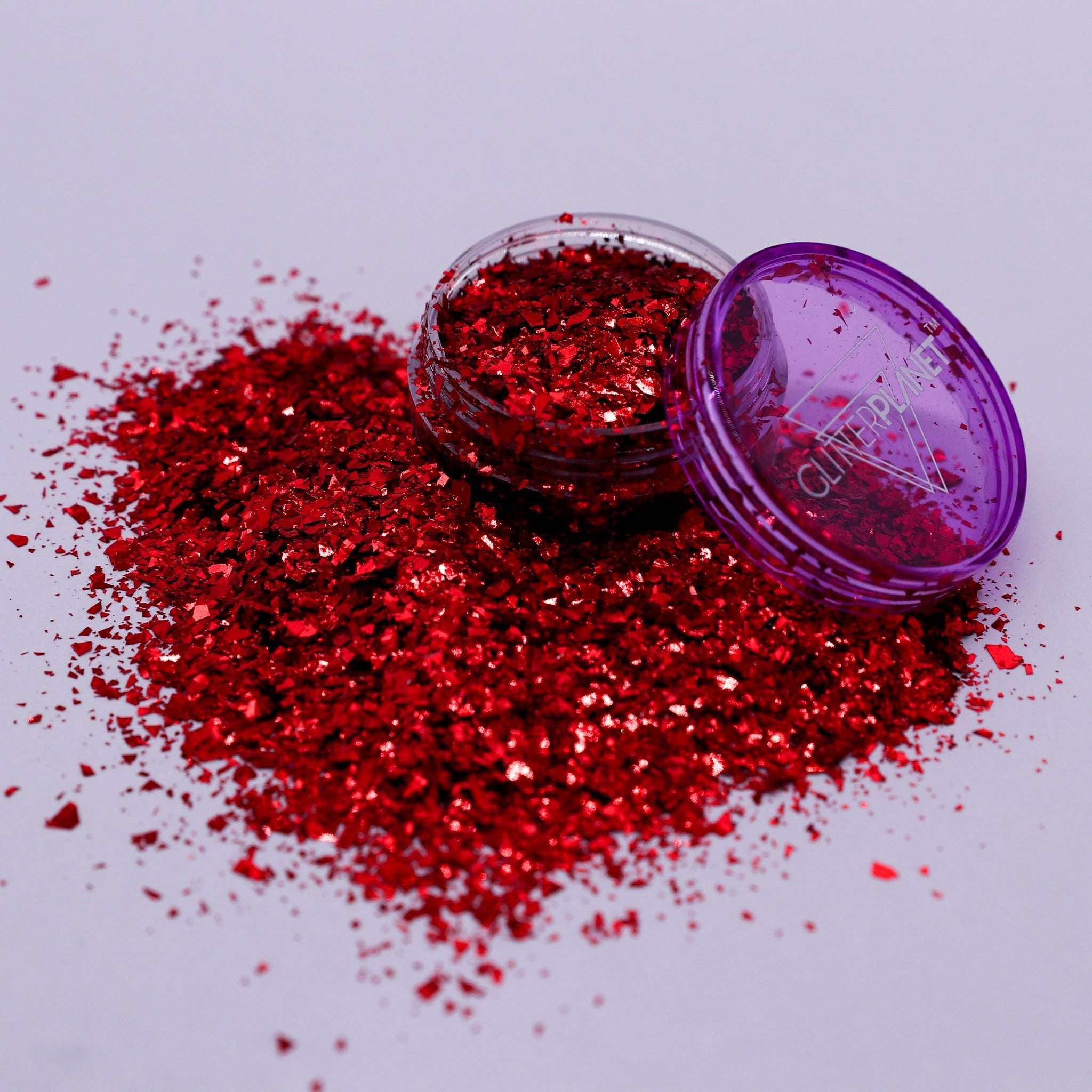 Red glitter spilling out of a purple container on a light gray background