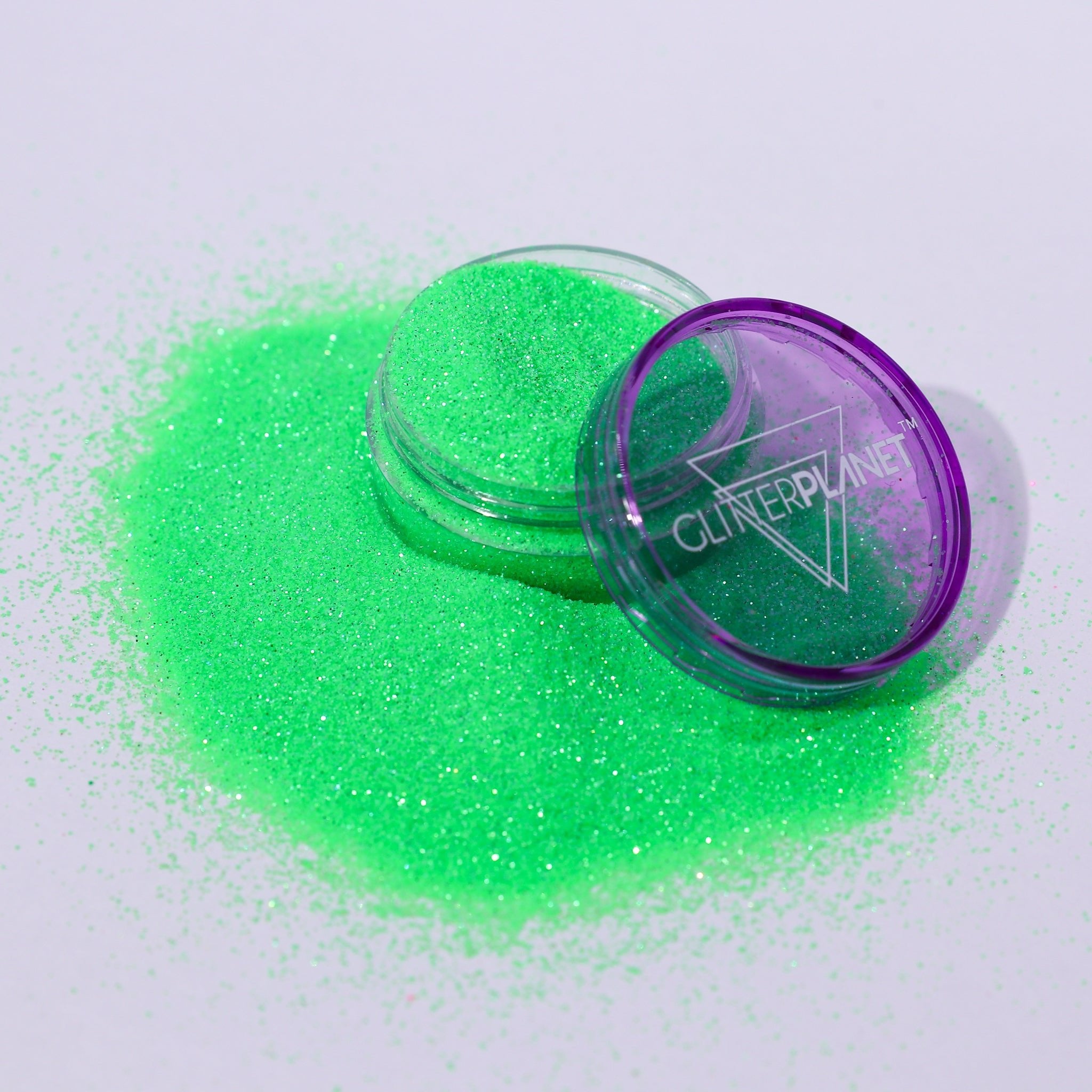 Green glitter in a clear container with a purple lid on a white background