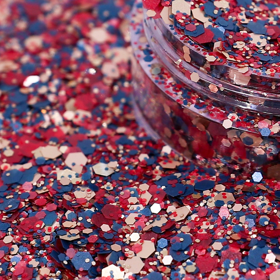 Colorful glitter with red, blue, and pink hex shapes spilling out of a container.