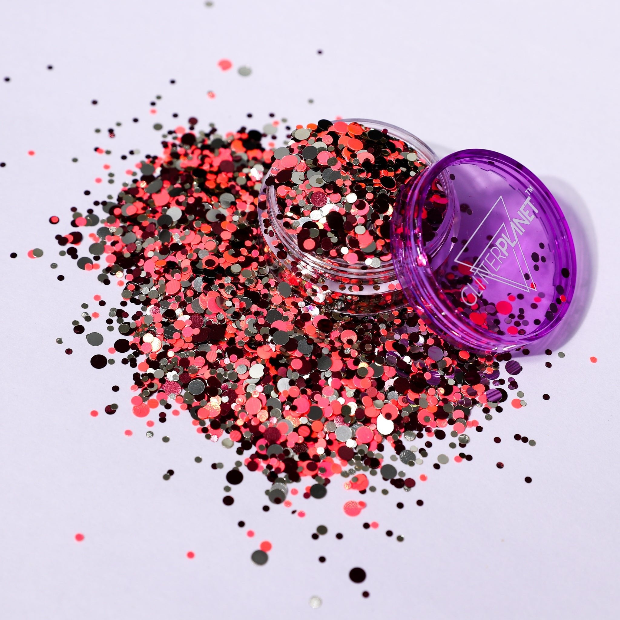 Colorful glitter spilling out of a purple container on a light gray background