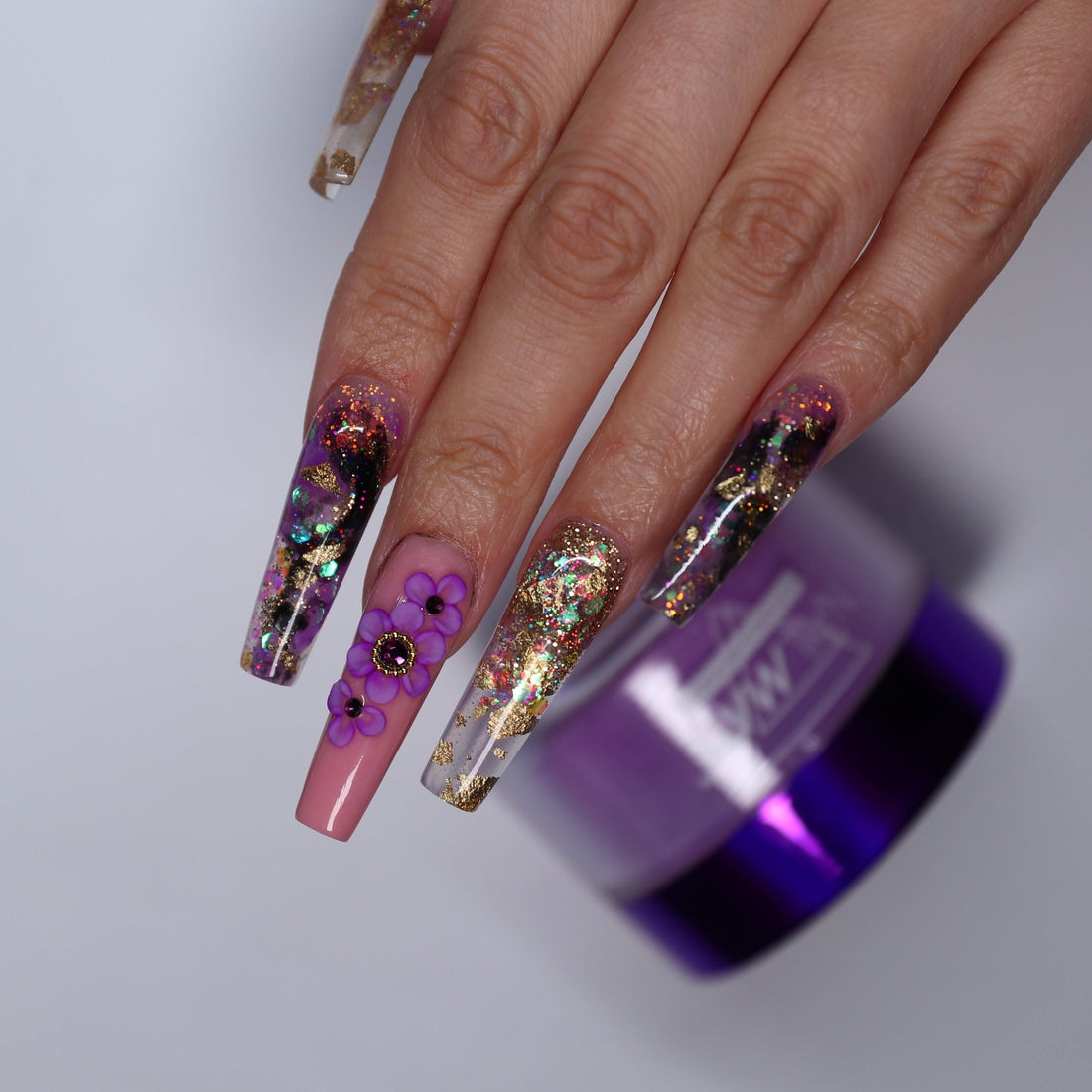 Hand with decorative nails holding a purple acrylic jar against a light gray background