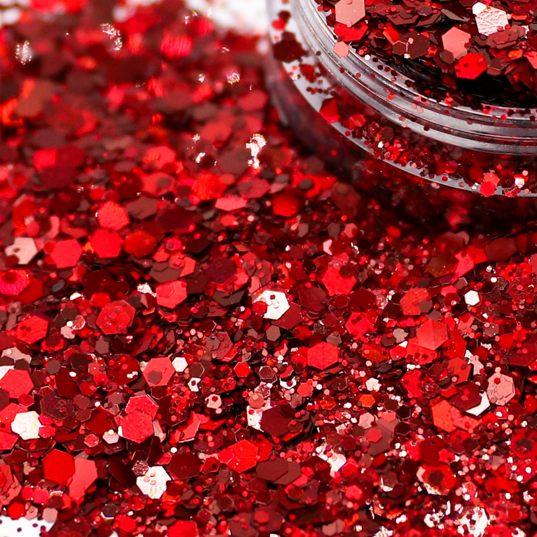 Close-up of red hexagonal glitter flakes spilled from a clear plastic jar, with the container partially visible at the top right.