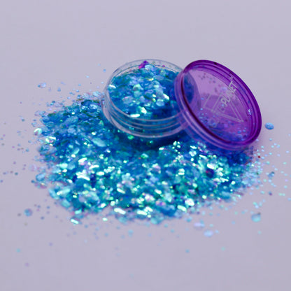 Blue glitter spilling out of a small open container with a purple lid on a light gray background.