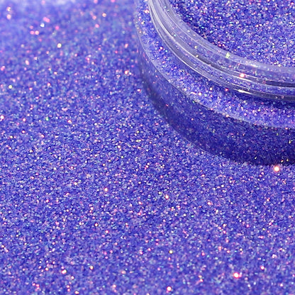 Close-up of purple glitter with a clear container partially filled with glitter.