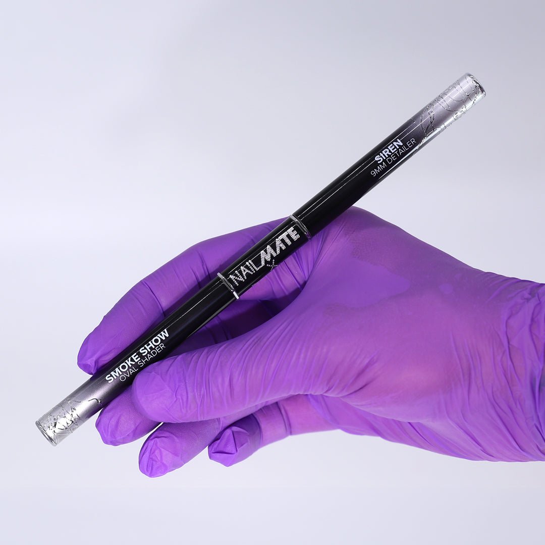 A hand wearing a purple nitrile glove holds a black dual-ended nail art brush labeled &
