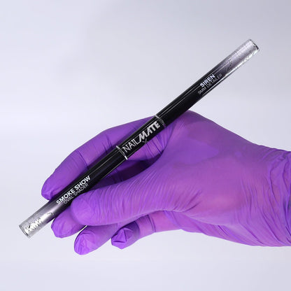 A hand wearing a purple nitrile glove holds a black dual-ended nail art brush labeled &