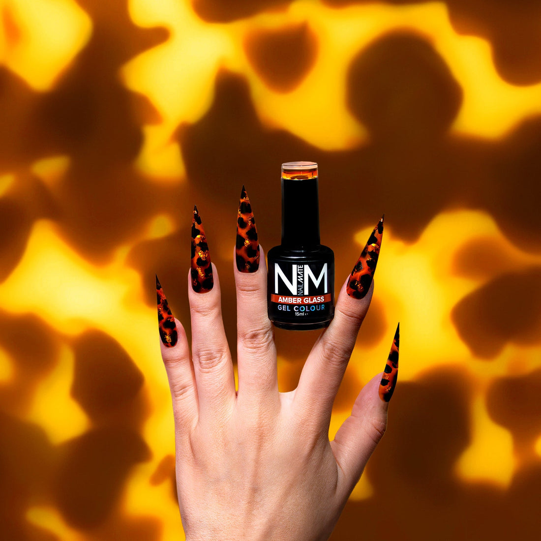 Hand with black and orange nail design holding a NAIL MATE gel polish bottle against a tortie patterned background