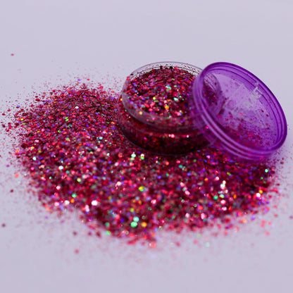 Pink glitter spilling out of an open purple container on a light gray background