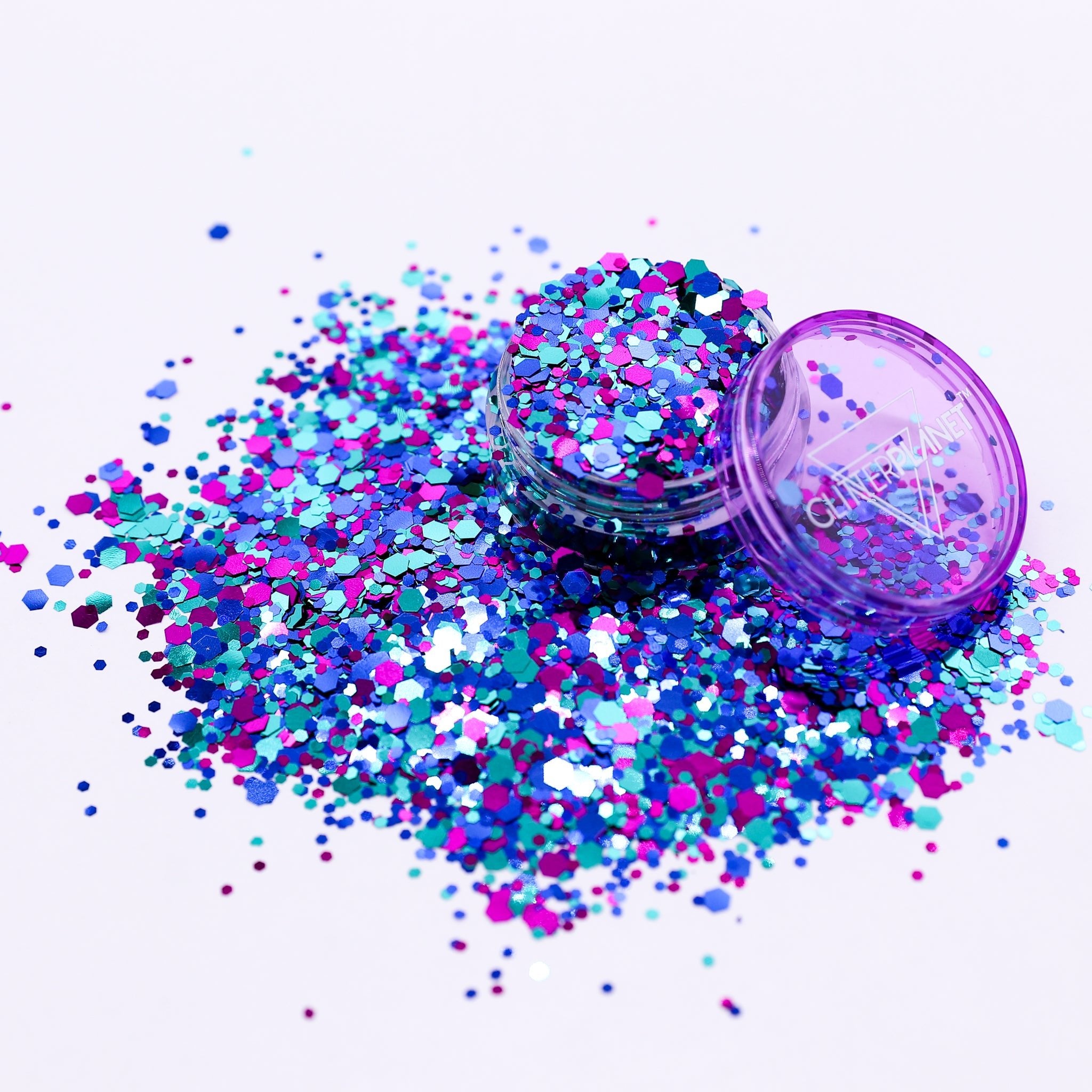 Colorful glitter scattered around an open purple container on a white background