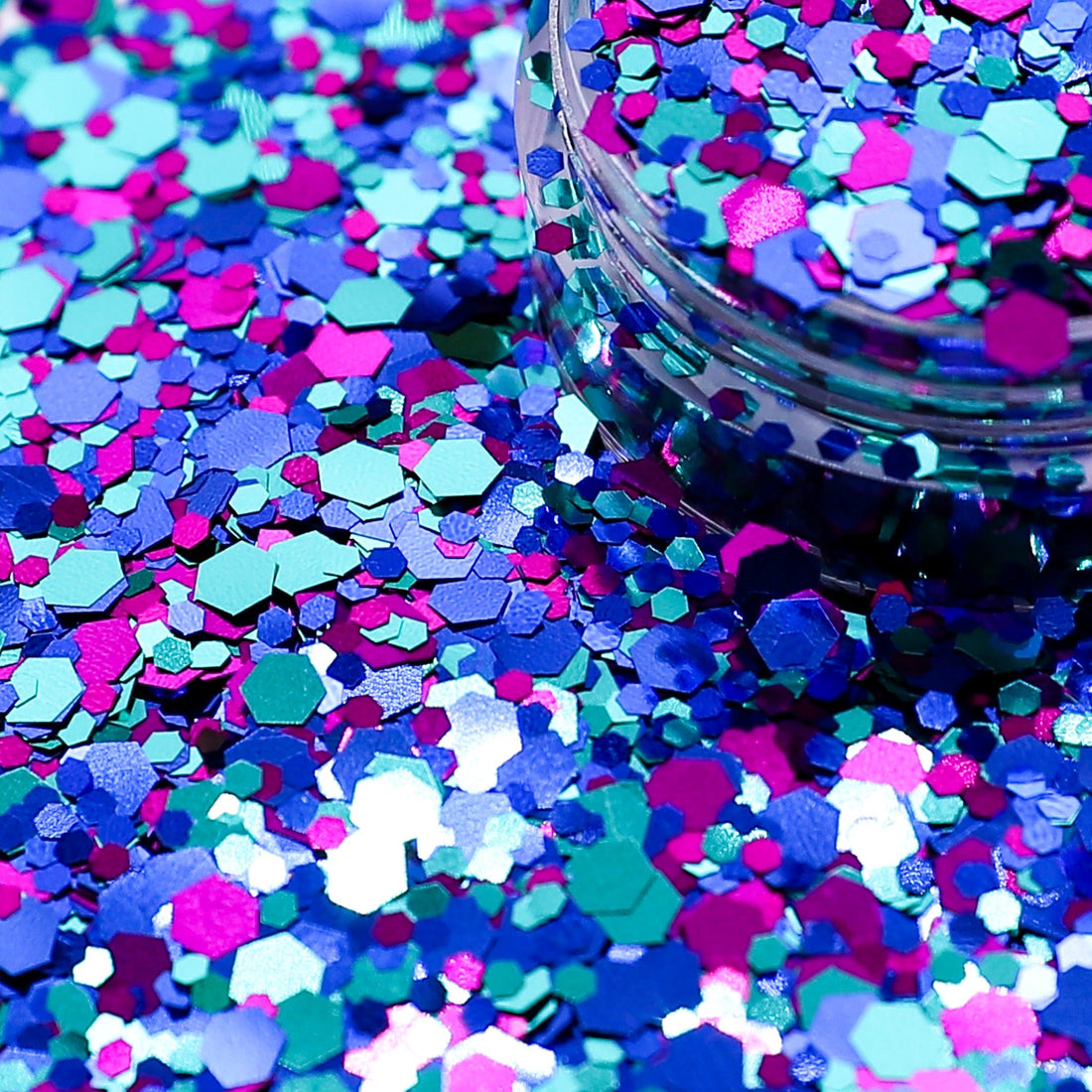 Colorful hexagonal glitter scattered on a surface with a container of glitter in the background.