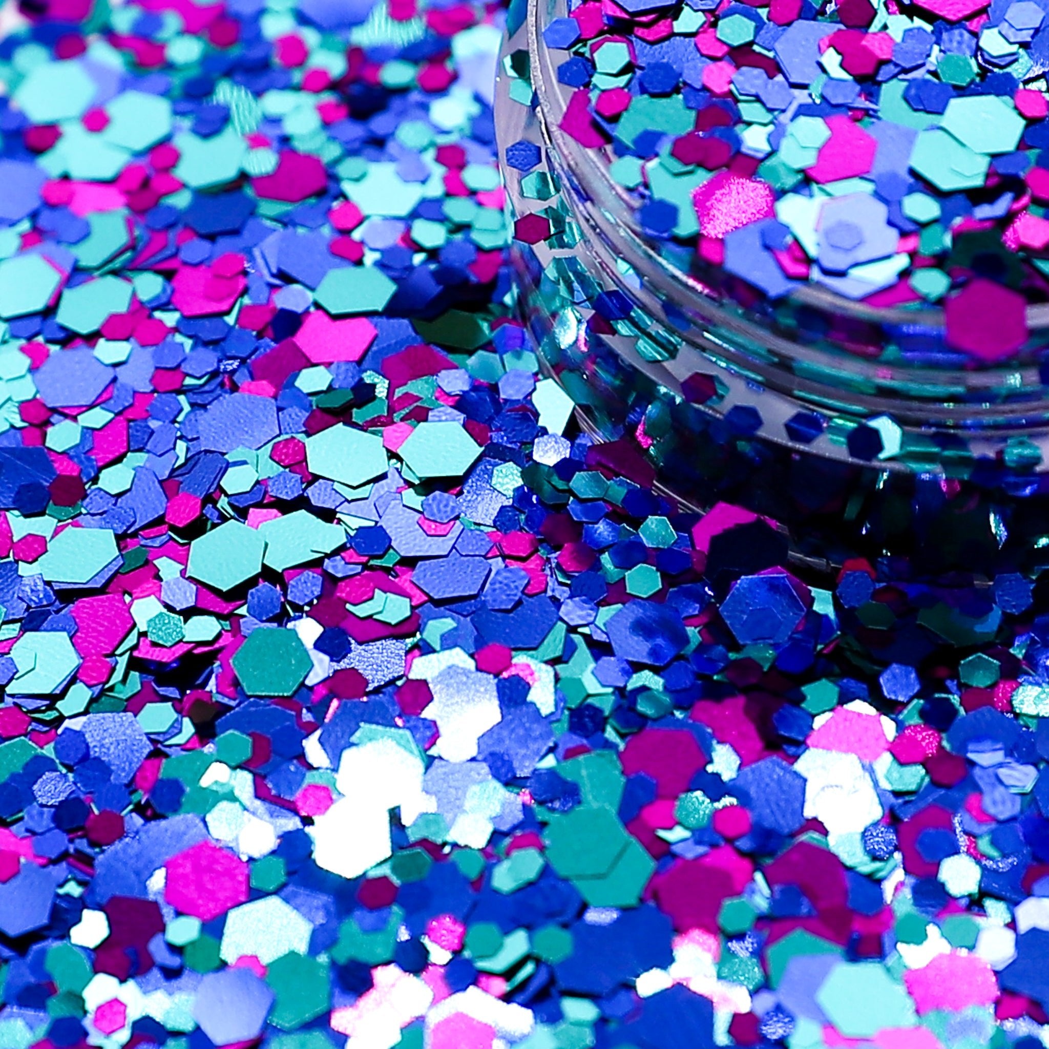 Colorful hexagonal glitter scattered on a surface with a container of glitter in the background.