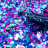 Colorful hexagonal glitter scattered on a surface with a container of glitter in the background.